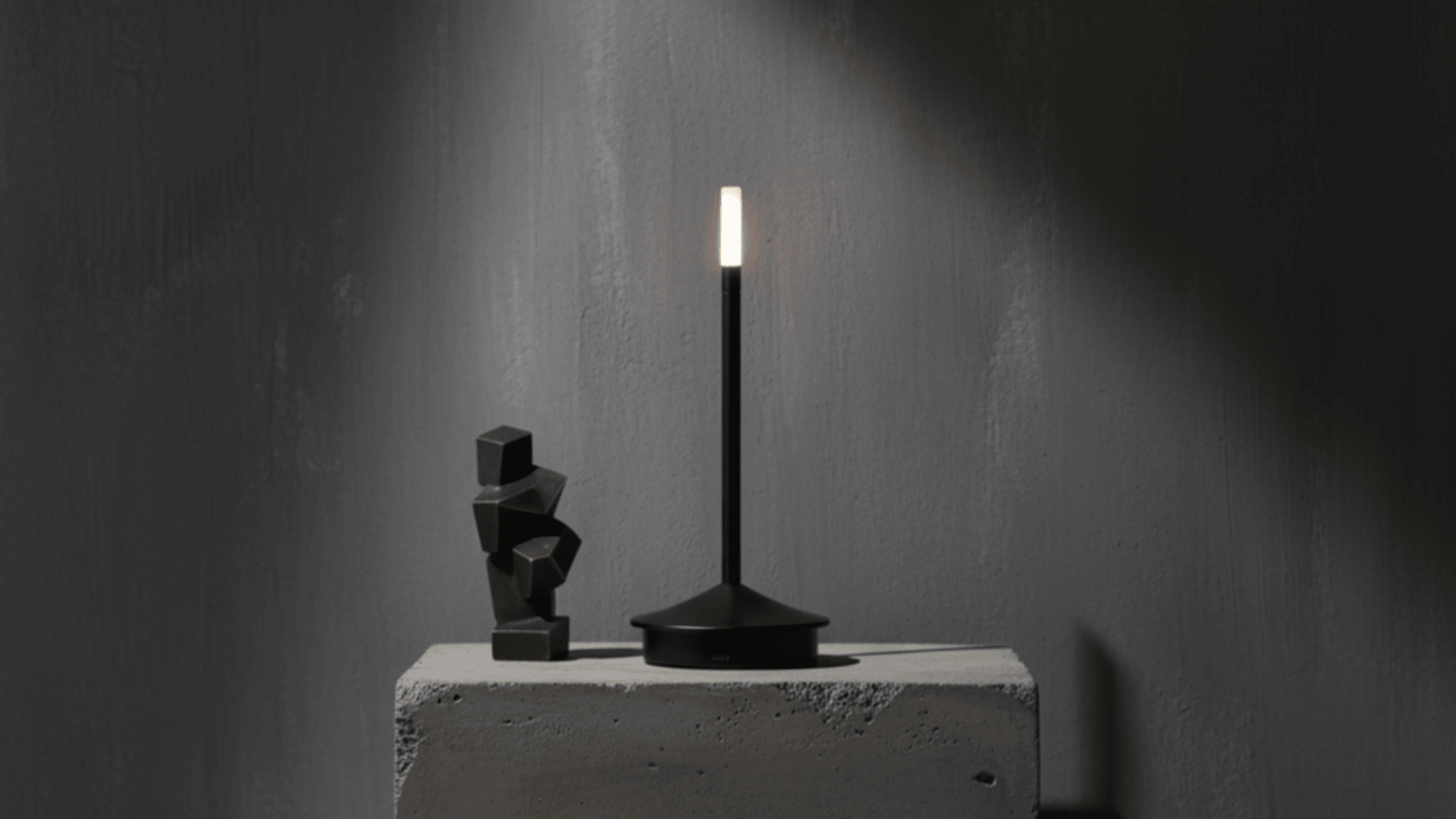 Modern black lamp and abstract sculpture on a concrete block against a dark wall.