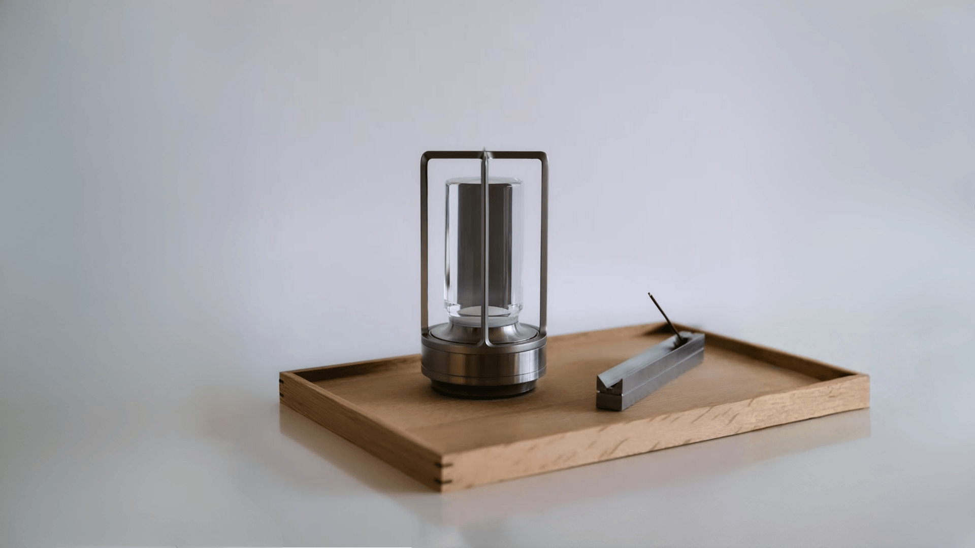 Modern lantern shaped lamp and a block of aluminum on a wooden tray with a white background