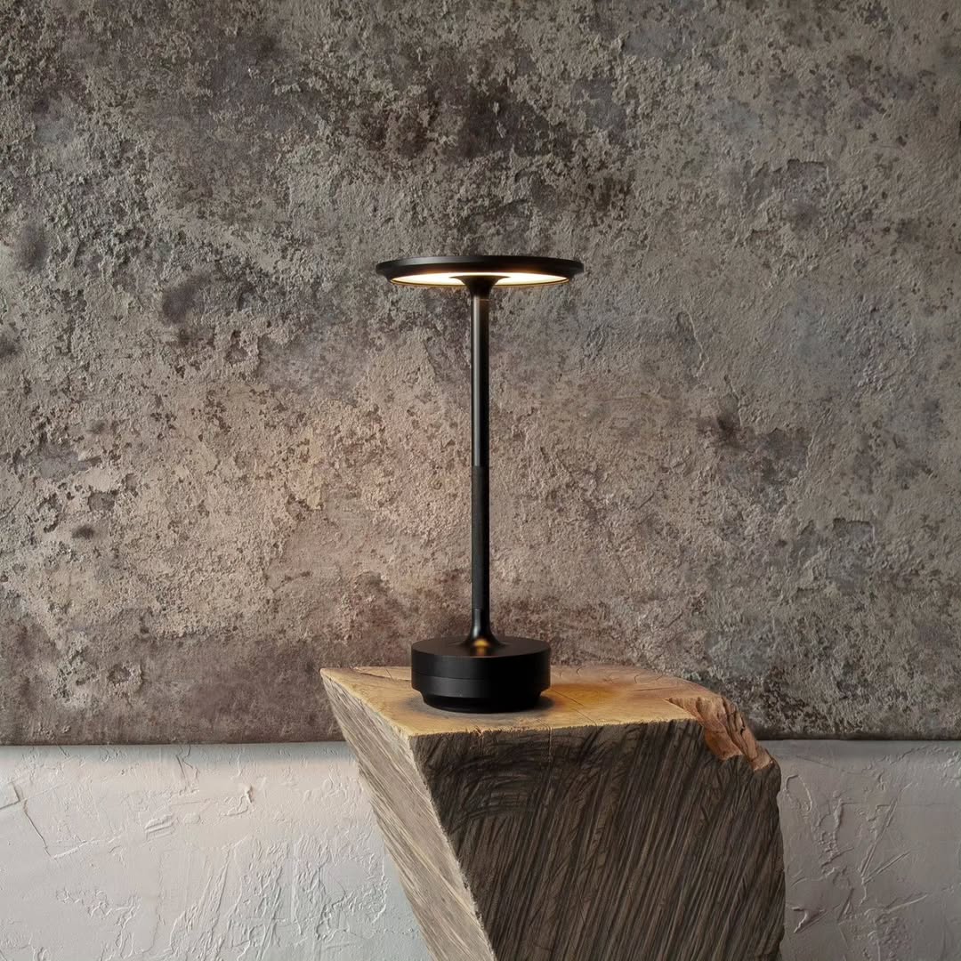 Modern black table lamp on a wooden block against a textured wall.